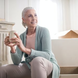 senior woman drinking coffee surrounded by moving boxes